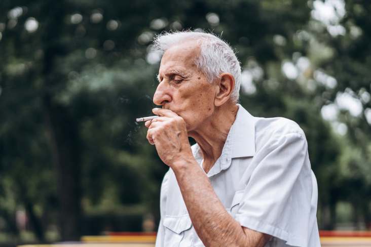 homem idoso fumando cigarro ao ar livre no parque da cidade